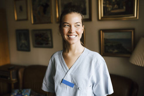 Happy female nurse looking away in living room - MASF27677