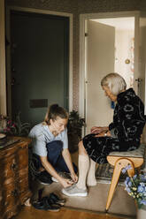 Eine Krankenschwester hilft einer älteren Frau, im Wohnzimmer zu Hause einen Schuh anzuziehen - MASF27679