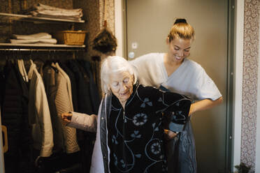 Lächelnde Krankenschwester, die eine ältere Frau auffordert, zu Hause eine Jacke zu tragen - MASF27682