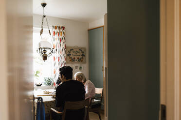 Junger Mann aus dem Gesundheitswesen trinkt Kaffee mit einer älteren Frau in der Küche zu Hause - MASF27701