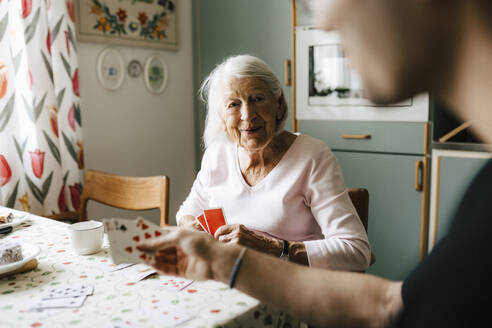 Elderly woman playing cards with male nurse at dining table - MASF27706