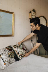 Männlicher Betreuer ordnet Kissen im Schlafzimmer zu Hause - MASF27715