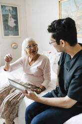 Elderly woman talking with male caregiver in bedroom - MASF27716