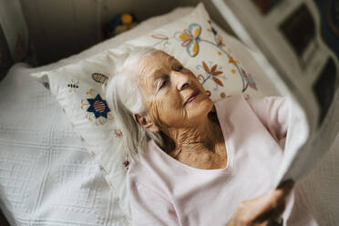 High angle view of senior woman reading newspaper while lying on bed - MASF27717