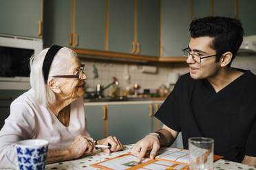 Lächelnde ältere Frau im Gespräch mit Pfleger in der Küche zu Hause - MASF27737