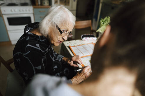 Ältere Frau im Gespräch mit einer Mitarbeiterin des Gesundheitswesens in der Küche zu Hause - MASF27743