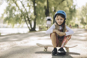 Girl with prosthetic leg looking down while sitting on skateboard in park - MASF27788