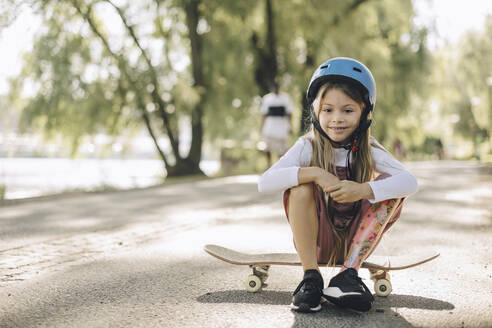 Mädchen mit Beinprothese schaut nach unten, während sie auf einem Skateboard im Park sitzt - MASF27788