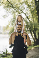 Porträt eines Vaters, der seine Tochter im Park auf der Schulter trägt - MASF27790