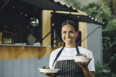 Happy female entrepreneur with food standing by truck - MASF27797