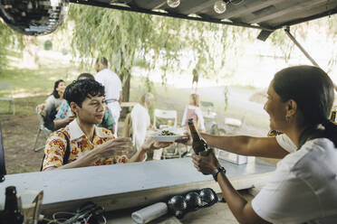 Female seller serving food to male customer at food truck in park - MASF27820