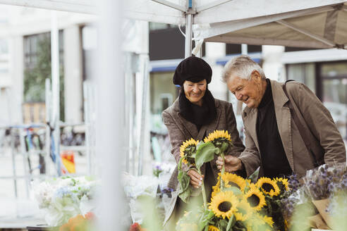 Lächelndes älteres Paar bei der Auswahl von Sonnenblumen auf dem Markt - MASF27830