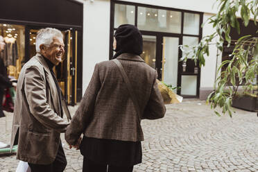 Happy senior man talking with woman while walking on street in city - MASF27848