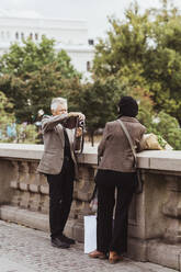 Senior man photographing woman through camera on bridge during weekend - MASF27851