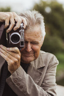 Elderly man photographing through camera during vacation - MASF27853