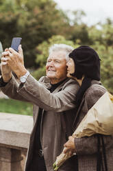 Frau küsst älteren Mann, der am Wochenende ein Selfie mit seinem Smartphone macht - MASF27855