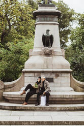 Älteres Paar verbringt seine Freizeit auf einer Bank vor einer Statue im Park - MASF27863