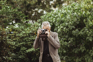 Älterer Mann fotografiert mit Kamera gegen Pflanzen im Park - MASF27868