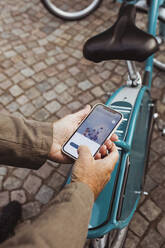 Abgeschnittene Hände eines älteren Mannes, der den QR-Code eines Fahrrads scannt, während er sein Smartphone an einer Parkstation benutzt - MASF27881