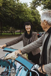 Lächelndes Seniorenpaar mit Elektrofahrrädern auf der Straße - MASF27883