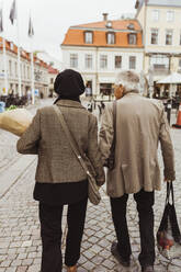 Rear view of elderly couple walking on street in city - MASF27896