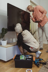 Männlicher Kunde im Gespräch mit einer Mitarbeiterin bei der Reparatur eines Fernsehgeräts im heimischen Wohnzimmer - MASF27924