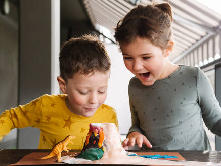 Adorable aufgeregt kleinen Jungen und Mädchen in Freizeitkleidung Blick auf ausbrechende Knetmasse Vulkan mit Erstaunen beim Spielen zusammen im Studio - ADSF32577