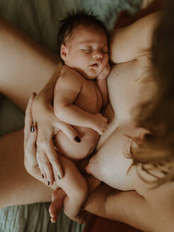 From above cropped unrecognizable peaceful young topless female in panties embracing adorable baby while sitting on bed after breastfeeding - ADSF32629