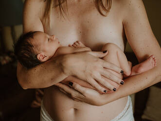 Cropped unrecognizable naked woman embracing adorable newborn after breastfeeding at home - ADSF32635