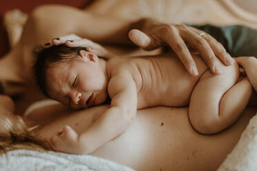 Cropped unrecognizable naked man embracing wife with newborn while lying down on bed after breastfeeding - ADSF32638