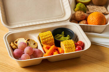 Von oben von Lunch-Boxen mit gesunden Lebensmitteln einschließlich Cracker Karottensticks Trauben Kirschtomaten mit Kiwi Brokkoli Walnuss und Mandarine auf gelbem Hintergrund - ADSF32658