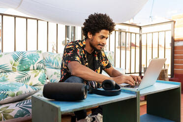 Afroamerikanischer Mann arbeitet an einem Netbook, während er auf einer Couch auf der Terrasse der Stadt sitzt - ADSF32684