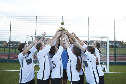 UK, Girls soccer team (10-11, 12-13) holding trophy in soccer field - ISF25501