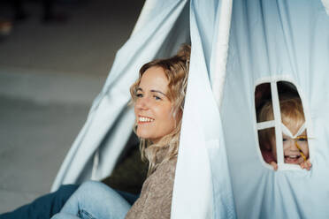 Mother sitting with girl and man in tent at home - GUSF06665