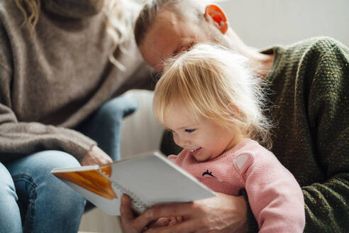 Tochter liest mit der Familie zu Hause ein Buch - GUSF06668