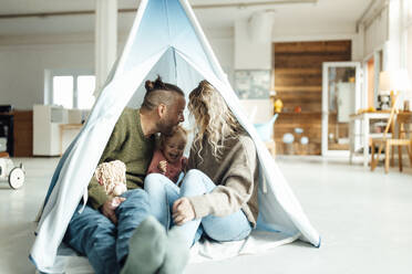 Playful daughter sitting inside tent with parents at home - GUSF06673