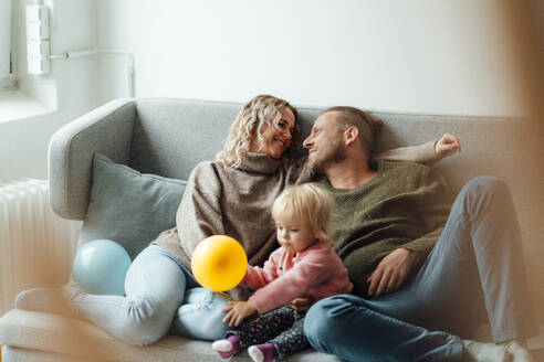Eltern schauen sich an, während ihre Tochter auf dem Sofa mit einem Luftballon spielt - GUSF06674