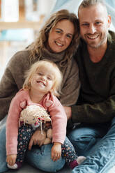Lächelnde Eltern sitzen mit ihrer süßen Tochter zu Hause - GUSF06676