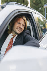 Lächelnder Geschäftsmann schaut aus dem Autofenster - JRVF02218