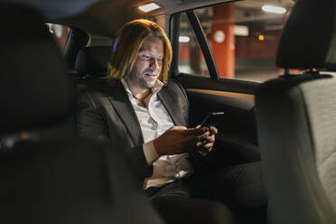 Geschäftsmann, der nachts im Auto ein Mobiltelefon benutzt - JRVF02225