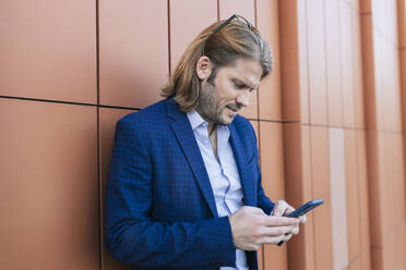 Businessman using mobile phone in front of wall - JRVF02234
