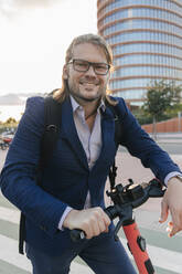 Businessman standing with electric scooter on road - JRVF02238