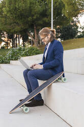 Businessman using laptop on steps by skateboard - JRVF02245
