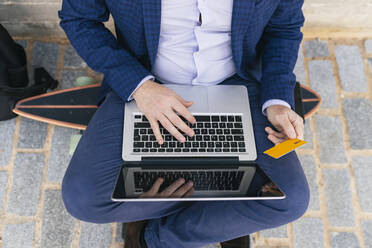Businessman with credit card using laptop on footpath - JRVF02248