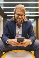 Smiling businessman using mobile phone at subway station - JRVF02258