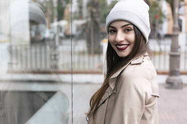 Young woman looking over shoulder near glass wall - JRVF02265