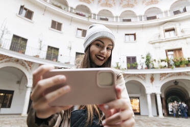 Frau macht Selfie mit Smartphone vor einem Gebäude - JRVF02270