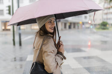 Smiling woman with umbrella standing at city street - JRVF02273