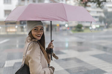 Frau blickt über die Schulter und hält einen Regenschirm auf die Stadtstraße - JRVF02274