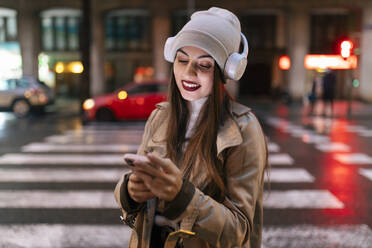 Junge Frau mit Kopfhörern und Smartphone in der Stadt - JRVF02299